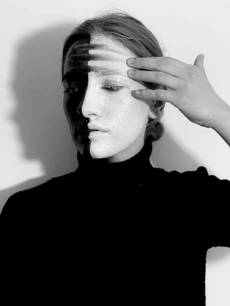 Woman with painted face, one side black and one white, smearing the black  into the white. 